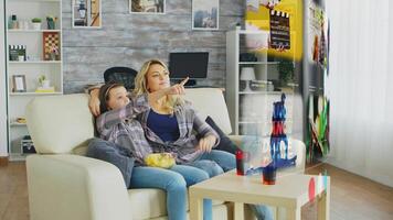 Parent and child relaxing in living room, watching online content on streaming services while enjoying snacks and beverages. Bored family picking what TV program to watch on media projector photo