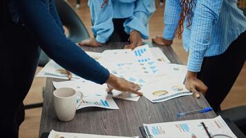 Employees making decisions in meeting, examining papers with commpany report and plans. People discussing about analytics to increase profit, business development solutions in agency office. photo