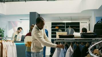 Young adult examining materials of formal wear hanging in clothing store at shopping center. Male client looking at trendy modern clothes or merchandise, buying fashion brands in retail shop. photo