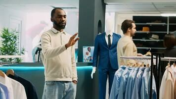 African american man looking at hologram in store, using augmented reality holographic image in fashion clothing boutique. Male customer checking clothes in shopping center. Tripod shot. photo