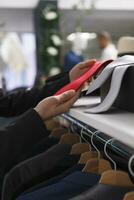 Clothing store woman seller hands touching red tie on shelf while checking merchandise in stock closeup. Shopping center mall boutique employee arms examining stylish accessory photo