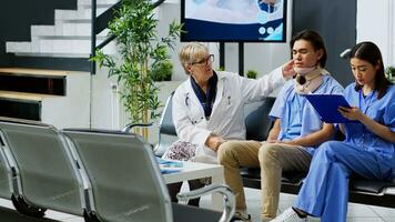 Senior doctor discussing medical expertise with nurse in hospital waiting area, explaining health care treatment to injured patient. Asian man wearing cervical neck collar during checkup visit photo