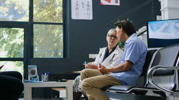 Senior doctor examining asian patient with glucometer during consultation, measuring insulin and glucose level from blood sample. Young adult doing diabetic control in hospital waiting area photo