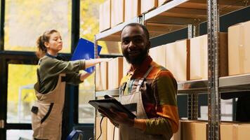 African american man using scanner in warehouse to scan barcodes on products stored in boxes. Male employee examining cargo merchandise on racks and shelves, reviewing logistics. photo