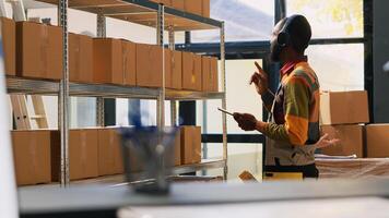 Young worker organizing products in depot, listening to music on headset while he works on quality control. Warehouse employee checking logistics on tablet, retail store delivery. photo