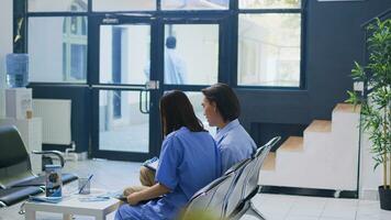 Nurse standing at hospital reception, writing medical expertise on clipboard. Asian patient calls the nurse to help him with insurance information during checkup visit examination in waiting area photo