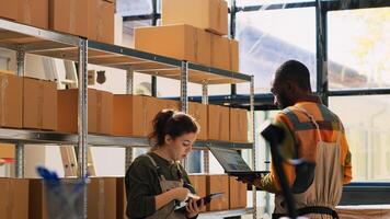 Storage room team verifying products in cardboard boxes, counting merchandise packages before shipping orders. Young diverse people working in storehouse, doing inventory. Handheld shot. photo