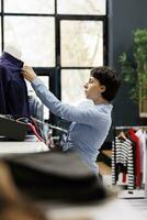 Clothing store worker arranging formal shirt on mannequin, preparing boutique for customers. Caucasian woman with short hair working with fashionable merchandise in shopping mall photo