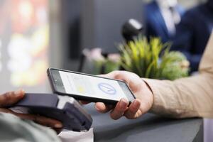 Female hand paying in clothing store with smartphone, tapping phone on contactless card reader while standing at cash register, close up. Customer using mobile phone as payment method in shopping mall photo