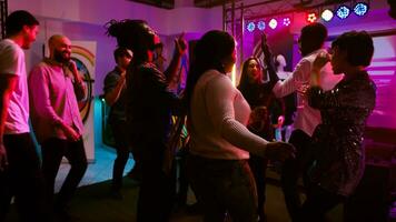 POV of woman dancing with friends on dance floor, having fun on night out and drinking alcohol. Cheerful girl partying with diverse people at nightclub or discotheque. Handheld shot. photo