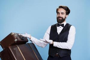 Young bellboy presents directions in studio, point to left and right for marketing advertisement campaign. Professional hotel porter showing sideways ad over colored background. photo