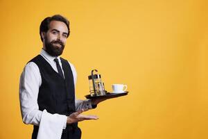 Elegant worker showing marketing ad while he holds platter with coffee cup and accessories. Professional waiter working at restaurant and presenting something to left or right sides. photo