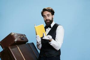 Bellboy recites poetry from book, wearing formal attire and enjoying lecture hobby against blue background. Hotel porter reading literature pages or novel story, classy staff member. photo