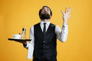 Employee praying to jesus for luck, asking for good fortune and being faithful. Spiritual religious skilled man working as waiter with food platter and formal clothes, feeling optimistic on camera. photo