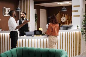 Hotel worker giving excellent service to guests at reception counter, talking about room accommodation after doing registration check in. Young man welcoming tourists at modern resort. photo