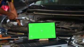 Close up shot of tablet placed on working bench in busy garage next to professional tools while technician mends vehicle. Mockup device in repair shop with meticulous specialist working in background photo