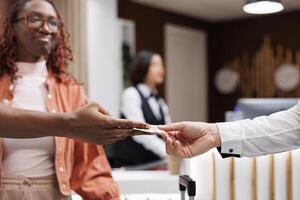 Young man giving money to steward at front desk counter in lobby, paying cash for services to carry trolley bags. Hotel bellboy receiving payment from guest, help with luggage. Close up. photo