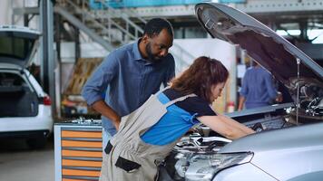 Engineer in garage cleaning opened up vehicle after replacing motor oil while customer watches. Car service worker doing inspection on automobile, wiping leftover leakage and talking with client photo