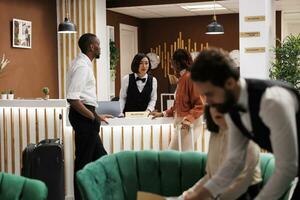 African american people talking to staff at front desk in hotel lobby, reviewing booking details and do check in process. Guests receiving warm welcome from receptionist at resort. photo