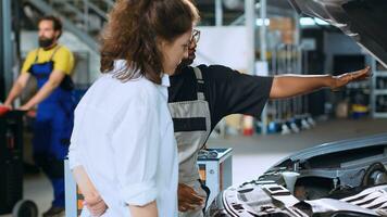 Helpful engineer assisting customer with car maintenance in auto repair shop. Licensed expert in garage looking over car components with woman, servicing her vehicle during annual checkup photo