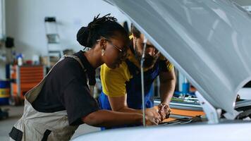 Coworking technicians in car service using torque wrench to fix damaged automobile. Man and woman in repair shop servicing broken vehicle, checking for faulty transmission using professional tools photo