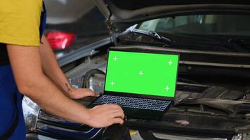 Engineer using green screen laptop in car service to order new parts for damaged vehicle. Close up shot of expert using chroma key device to look online for components to replace old ones photo