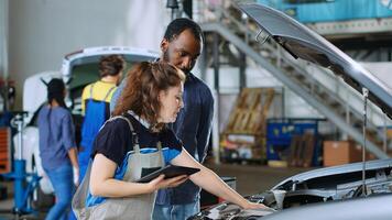 Mechanic in car service uses tablet to calculate repairments invoice for client after fixing broken components. Auto repair shop worker uses device to inform man of final costs after repairing vehicle photo