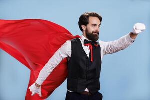 determinado adulto posando como superhéroe mientras él usa rojo manto en contra azul antecedentes en estudio, profesional persona interino me gusta un sobrehumano. hombre con formal atuendo y dibujos animados capa. foto