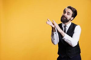 Happy waiter in suit claps hands to congratulate someone on new achievement, giving confidence boost in studio. Young man applauding person while he works as butler at restaurant, cheering. photo