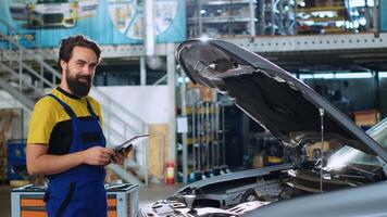 retrato de sonriente mecánico en auto reparar tienda haciendo coche anual chequeo, mirando para daños y perjuicios. contento reparador a trabajo comprobación a ver Si vehículo partes son correctamente marcha foto