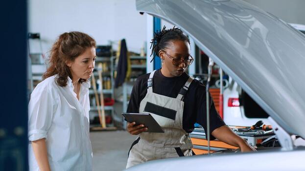 Certified engineer in car service using tablet to calculate repairments invoice for client after fixing malfunctions. Trained professional using device to determine final costs after servicing vehicle photo