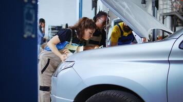 Team of mechanics in car service using inspection lamp to fix automobile in need of repairments. Colleagues service broken vehicle, checking for faulty engine using professional tools, dolly out shot photo