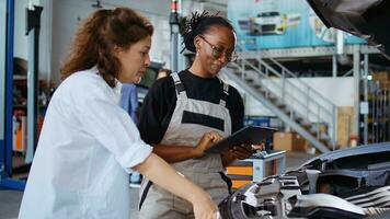 Helpful mechanic in garage using tablet to follow checklist while doing maintenance on car, talking with client. Professional in auto repair shop does checkup on vehicle next to customer photo