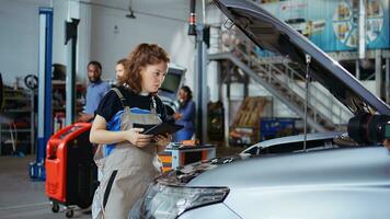 Certified mechanic in repair shop using laptop to check car performance parameters during maintenance. Specialist using device in garage to examine damaged vehicle, zoom out shot photo