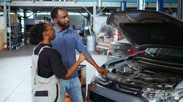 Cheerful engineer in repair shop using tablet to check car performance parameters during inspection. Relaxed garage workspace employee using device to examine damaged vehicle photo