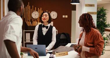 Friendly receptionist presenting holiday package options to african american couple in posh hotel. Husband and wife on honeymoon trip preparing to pay for extra room amenities in resort lounge photo