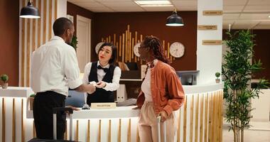 Friendly bellhop employee showing tourists the way to their room while carrying luggage after check in process is over. Stressed hotel manager verifying guests booking paperwork photo