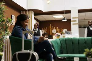 Smiling African American hotel staff standing at front desk welcoming and greeting guests with smile. Friendly female receptionist waiting for tourists, good customer service in hospitality photo