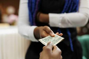 Close up of hotel employee wearing uniform holding money cash taking payment from customer while working in hospitality industry, selective focus. Waitress receiving tip from generous client photo