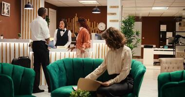 Busy hotel manager receiving cup of coffee from employee while checking paperwork of guests waiting to be checked in. Receptionist offers room access to couple after booking process is finalized photo