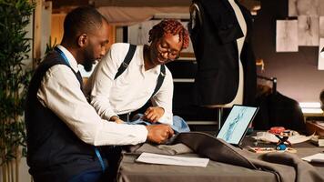 Tailor and assistant picking fabric to create modern clothes, working in atelier to craft clothing items for fashion collection. Two designers choosing material, handmade. Handheld shot. photo