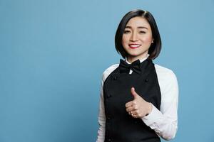 Smile waitress showing thumb up gesture, expressing happiness and confirming approval portrait. Catering service woman employee standing with like symbol and looking at camera photo