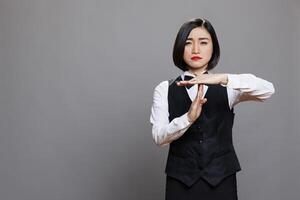 Confident asian waitress wearing uniform showing timeout sign with arms portrait. Restaurant serious woman employee asking to take break while making gesture with hands and looking at camera photo