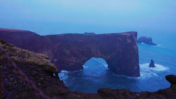 Rock stone gate on dyrholaey peninsula with majestic spectacular landscape, foggy rock cliff. Beautiful coastline stone arch near reykjavik iceland. Scenic wilderness art. Handheld shot. photo