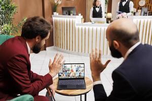 Management team attend videocall together in reception of luxury hotel, meeting with coworkers while they are travelling on business trip. Two managers in lounge area using videoconference call. photo