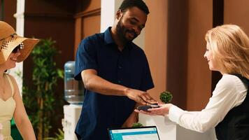 turistas pago para habitación alojamiento a complejo, utilizando crédito tarjeta en pos terminal a frente escritorio recepción vestíbulo. personas en Luna de miel vacaciones haciendo pago sobre su llegada. Mano disparo. foto