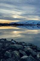 Scandinavian frosty lake near highlands forming nordic winter landscape at sunset, large body of water and snowy mountains in icelandic scenery. Frozen fields in spectacular countryside. photo