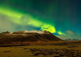 Aurora borealis y masivo montañas en Islandia. brillante del Norte luces creando increíble nórdico paisaje debajo estrellas en cielo. vistoso mágico fenómeno con sierras, noche fotografía. foto