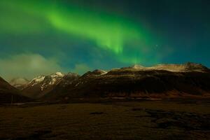 islandés paisaje con del Norte luces cubierta Nevado montaña tapas, noche fotografía. nórdico Aurora borealis esclarecedor estrellado cielo con verde y azul, paisaje con cautivador panorama. foto