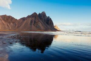 Towering alpine vestrahorn hills, icelandic fantastic environment on peninsula of Stokksnes. Overview of scandinavian nordic scenery with lovely black sand beach in frozen Iceland. photo